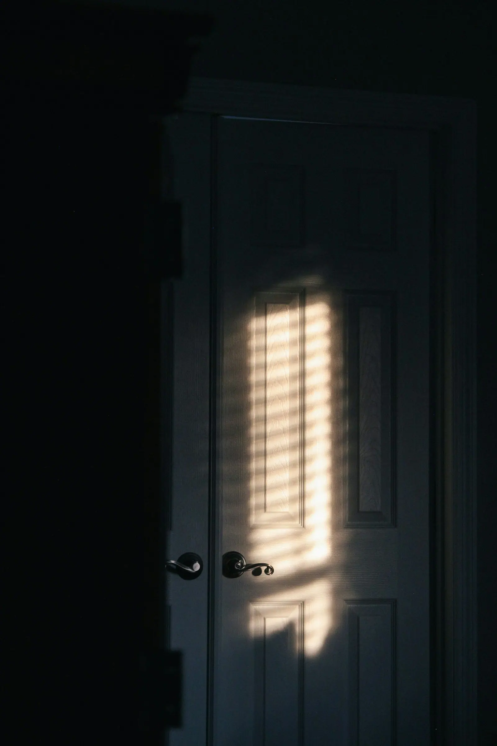 Luz filtrada por una contraventana sobre una puerta cerrada